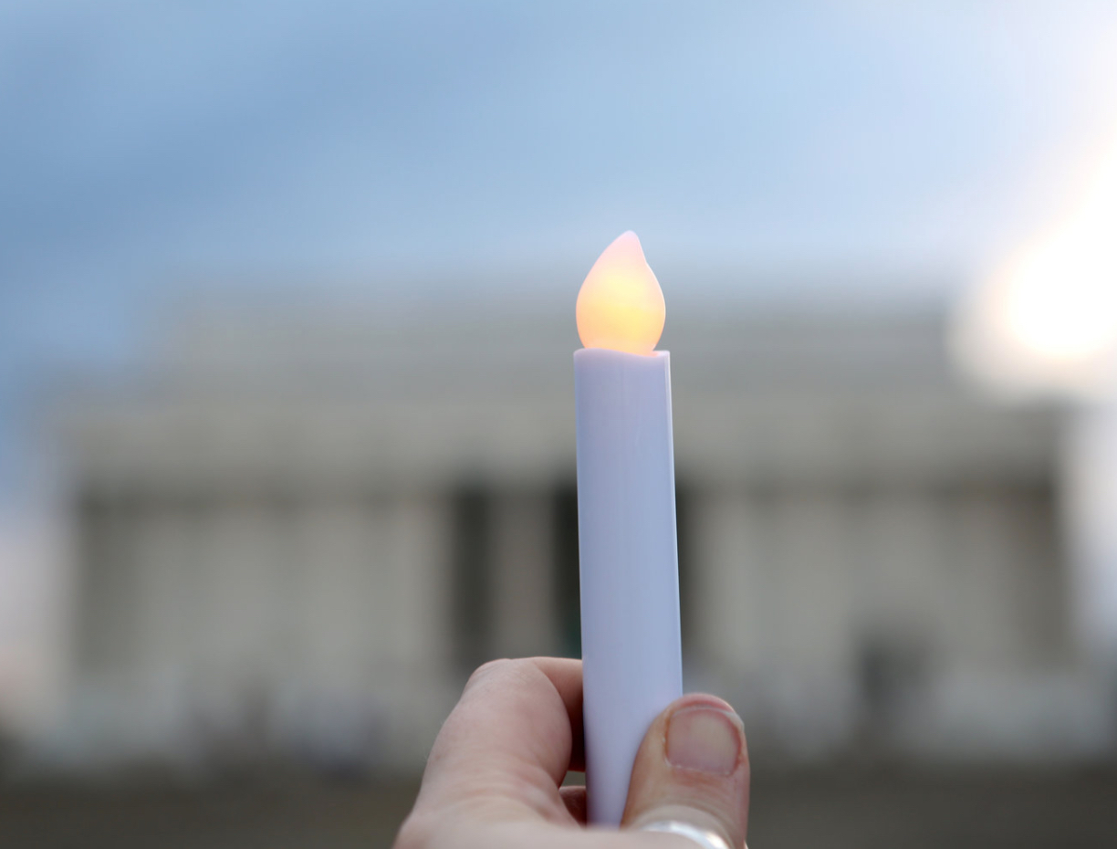 A candle is held in focus with the out of focus Lincoln Memorial in the background.